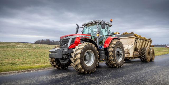 Massey Ferguson 7S high-horsepower tractor towing a large manure spreader on a rural road